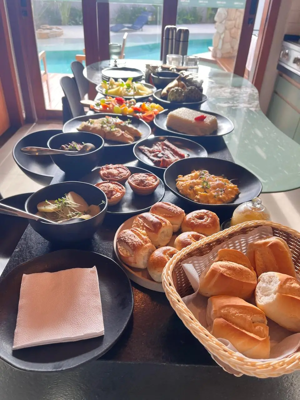 Mesa de buffet montada à beira da piscina, com travessas escuras variadas